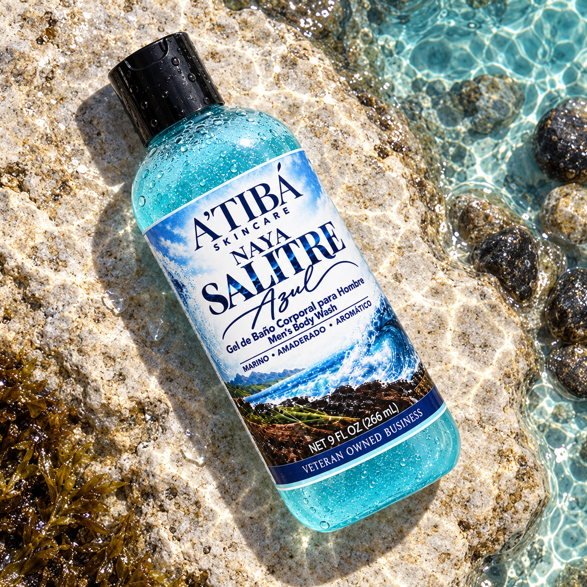 NAYA Salitre Azul Men's Body Wash by A'TIBÁ Skincare — overhead shot of clear 9 oz bottle with deep blue gel resting on wet coastal rocks beside turquoise Caribbean water, Veteran Owned Business, Yauco Puerto Rico